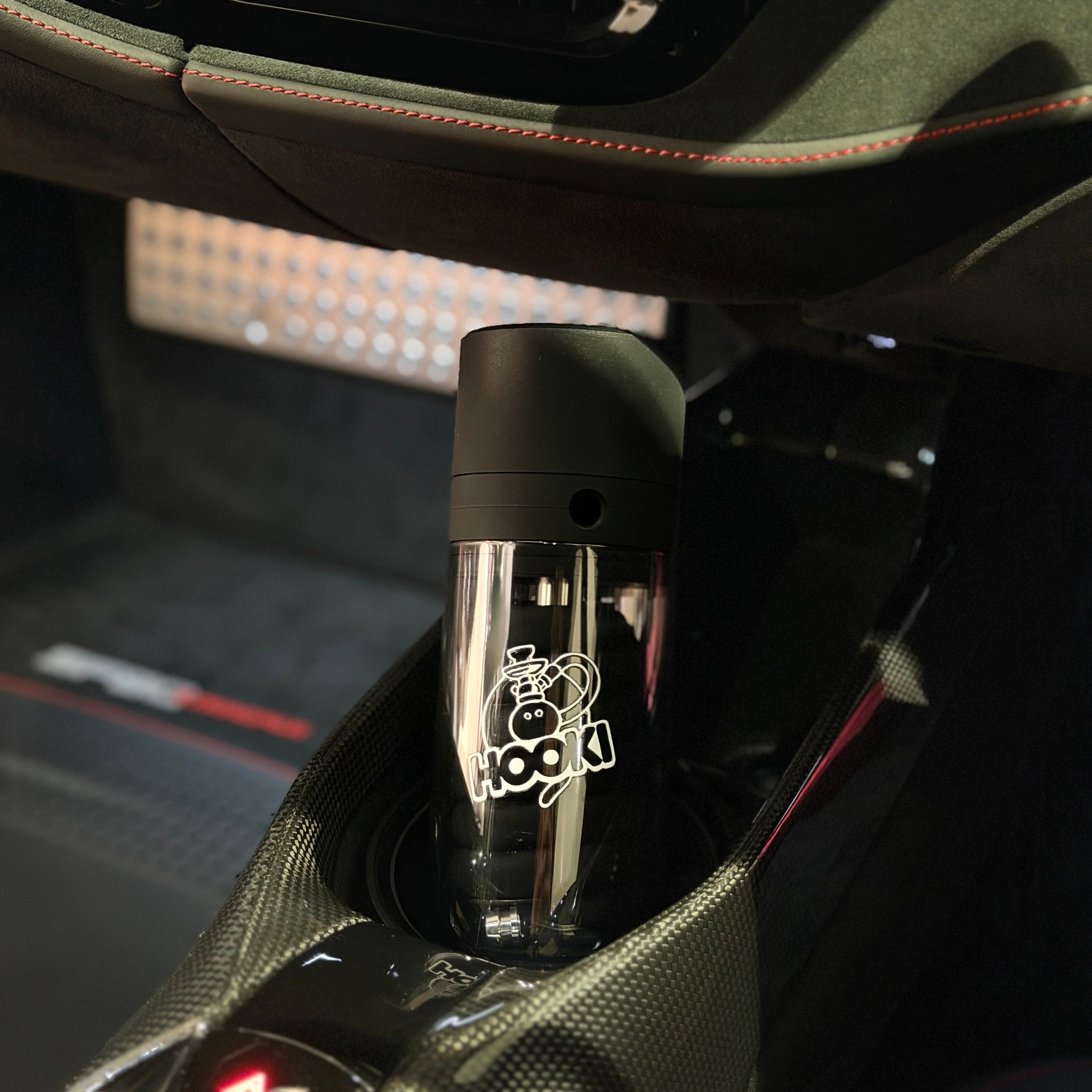 A mini portable hookah placed in a car cup holder inside a ferrari interior.